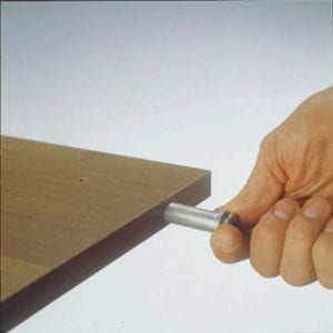 A person using a CONCEALED LEVELERS DRILL TEMPLATE to level a wooden table.