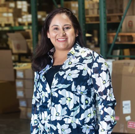 Meet The Team: a woman in a floral shirt standing in a warehouse.
